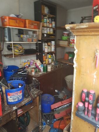 Werkstatt mit Regalen voller Werkzeug, Farbeimer, Schraubenziehern und Arbeitsmaterialien.