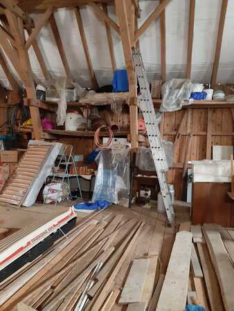 Eine Dachbodenwerkstatt mit Holz, Werkzeugen, Regalen und Baumaterialien im Rohbau.